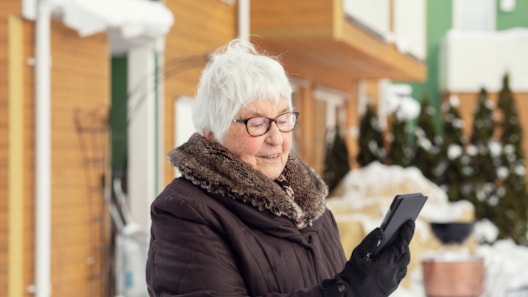 eldre kvinne ser på mobiltelefon utendørs