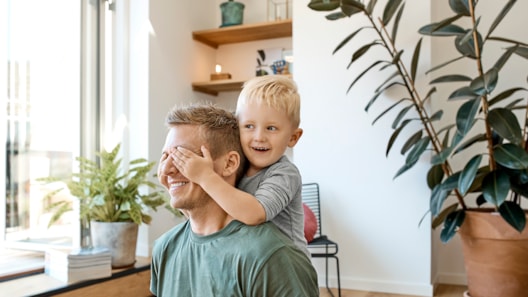 Liten smilende gutt holder hendene øynene på faren sin