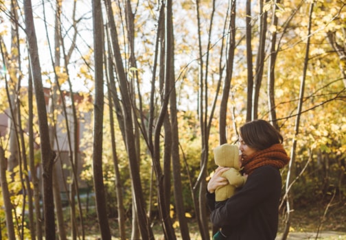 Kvinne med skjerf som bærer barn ute i en skog om høsten