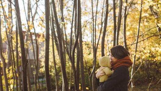 Kvinne med skjerf som bærer barn ute i en skog om høsten