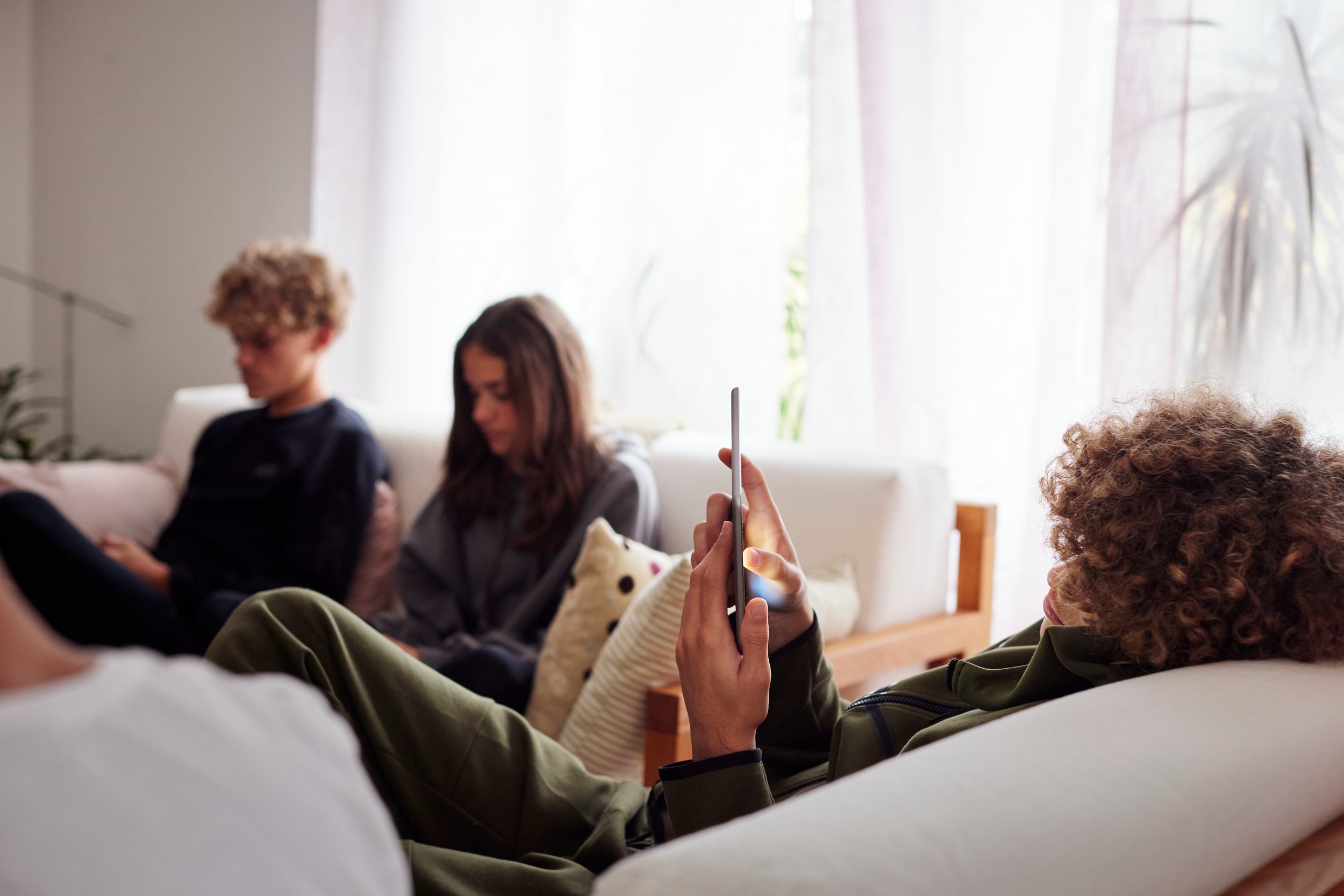 Gruppe unge som sitter inne i en sofa med telefon i handa