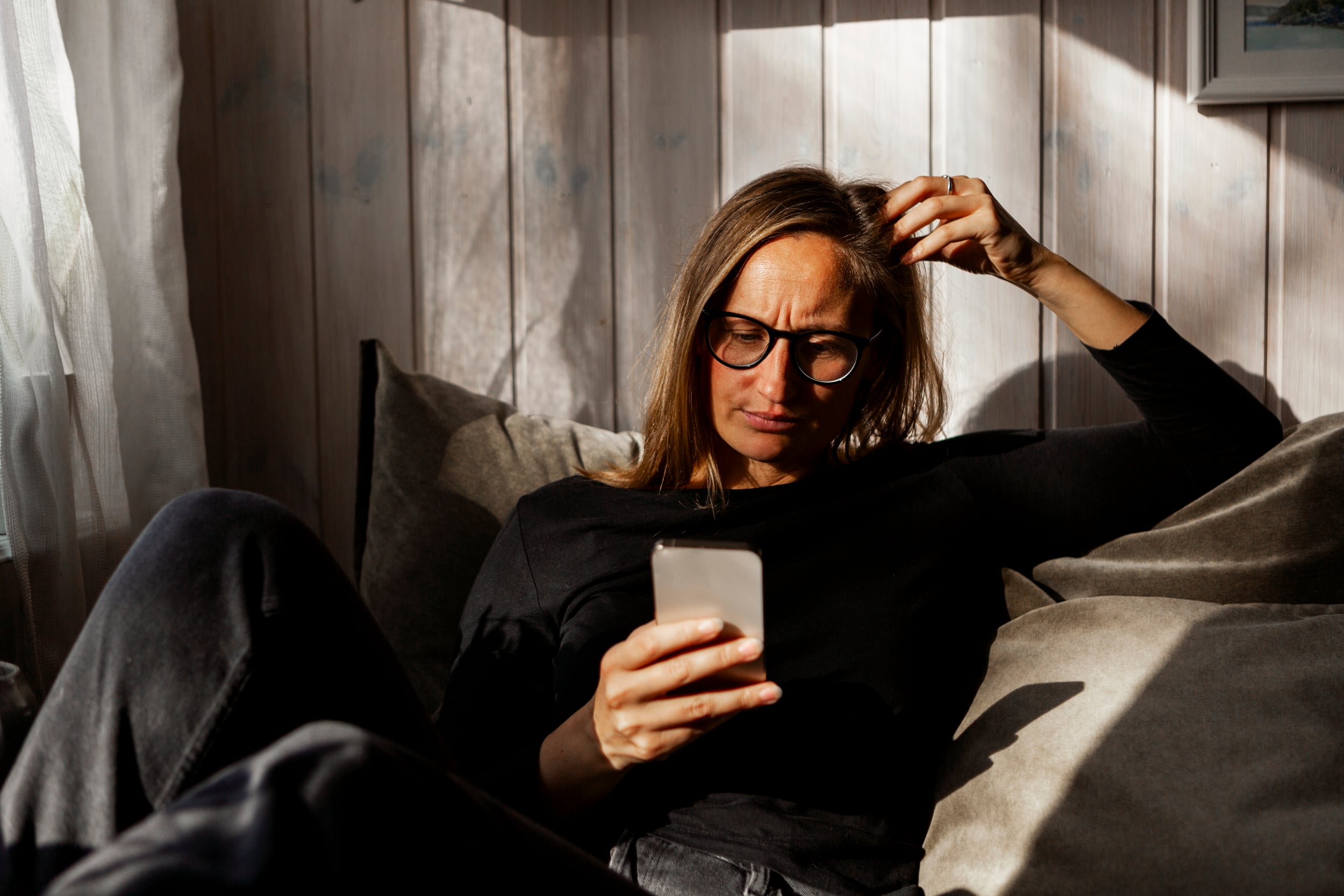Kvinne som sitter innendørs i en sofa og ser ned på en mobiltelefon.