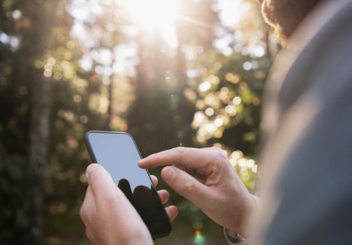 Mannlige hender som holder en smarttelefon utendørs.